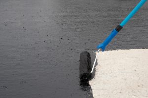 A close-up of a roller brush applying waterproofing coating on concrete